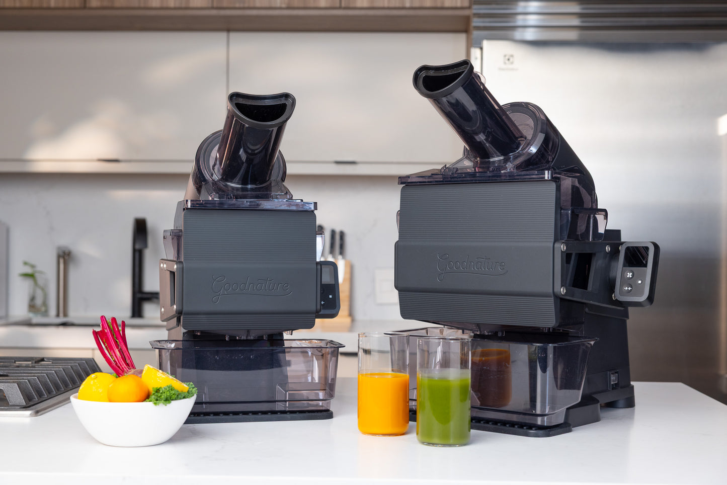 Two commercial juicers on a counter with cold pressed juice in the foreground.